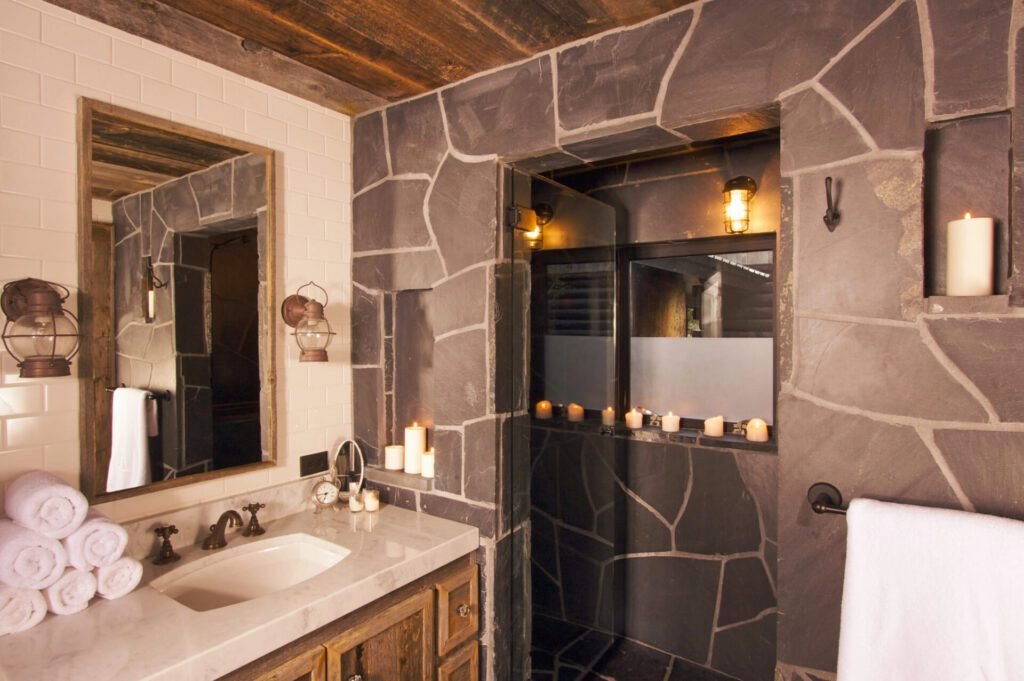 Earthy-tone bathroom with natural wood accents, stone finishes, candles, and lantern-style lights above the sink.