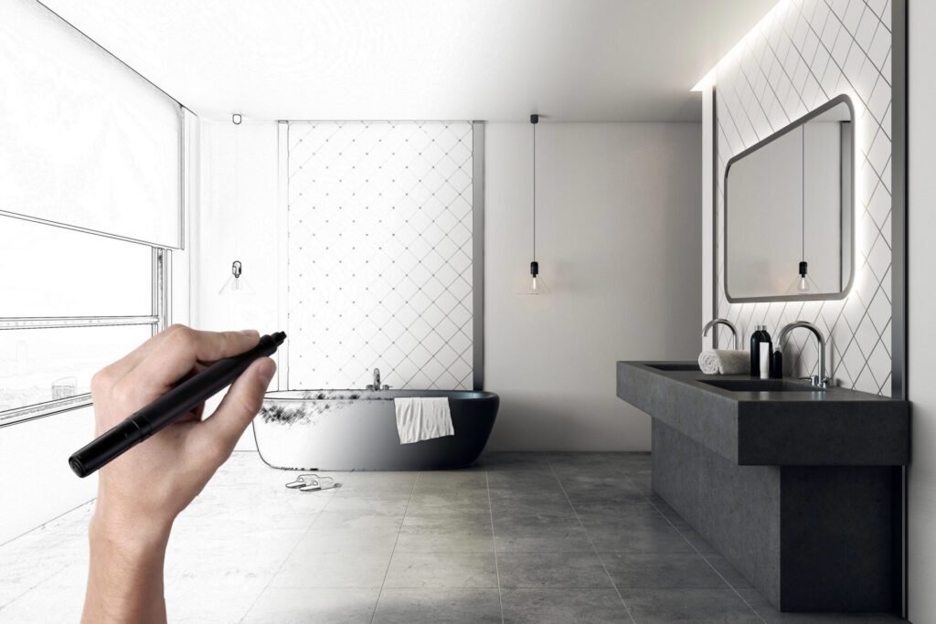 Before-and-after bathroom image showing a hand drawing the design on the left and a modern finished bathroom with a flat black tub, dual vanity, dark grey tile, and pendant lighting on the right.