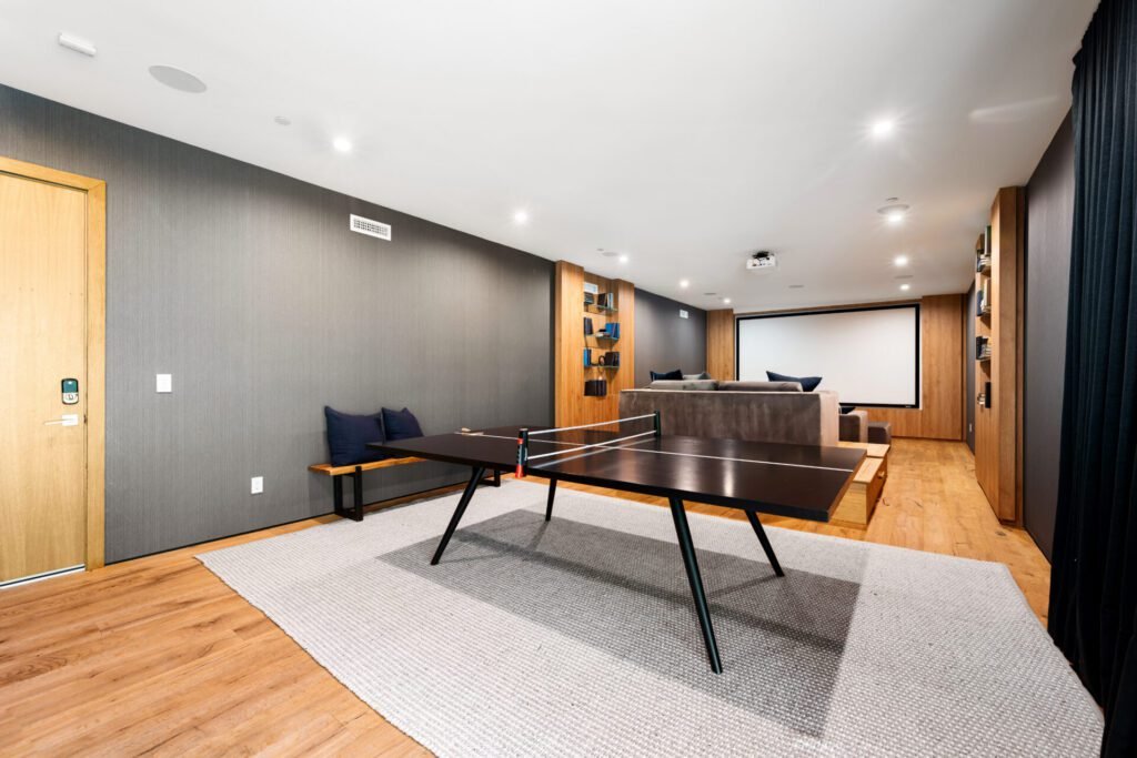 Finished basement with dark grey walls, wood accents, area rug, ping pong table, couch, and projector