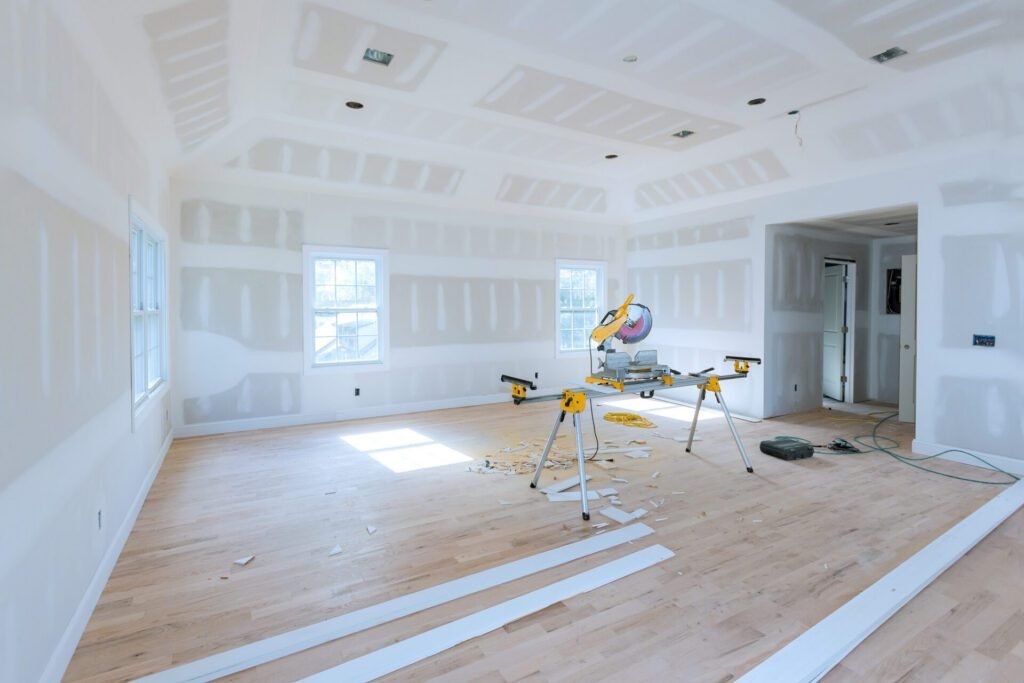 Large open room during a remodel, with new drywall installation and construction materials on site.