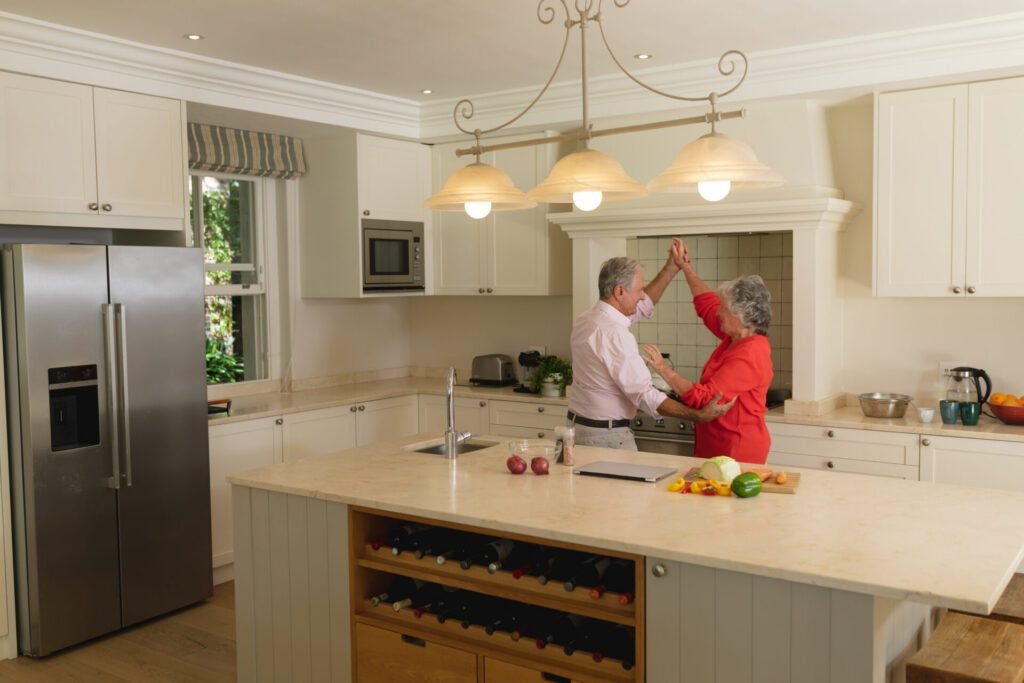 Senior couple dancing and smiling in their newly remodeled kitchen with warm lighting.